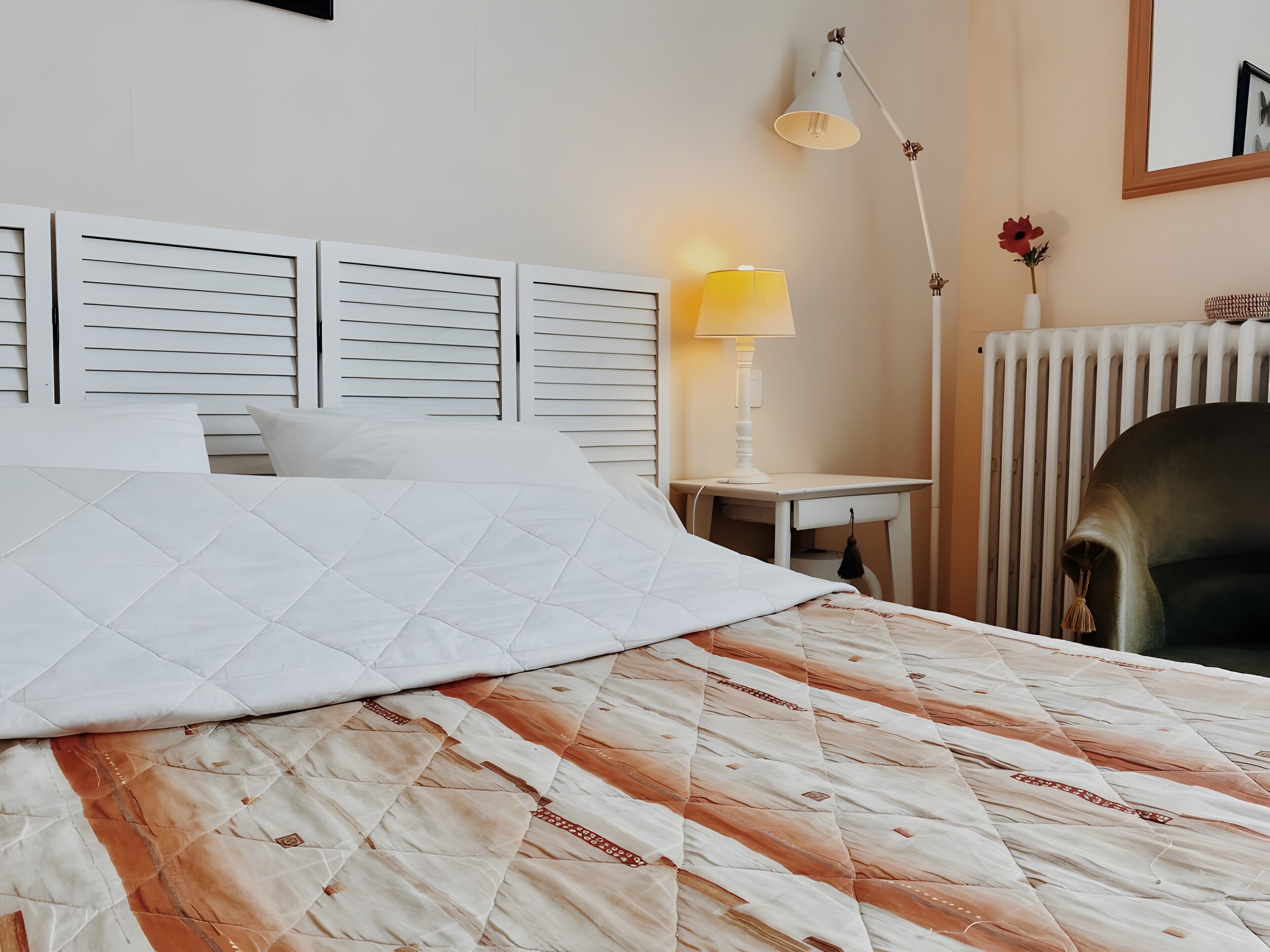 Une chambre d’hôtel avec un lit, une table de chevet, une lampe, une chaise et un radiateur.