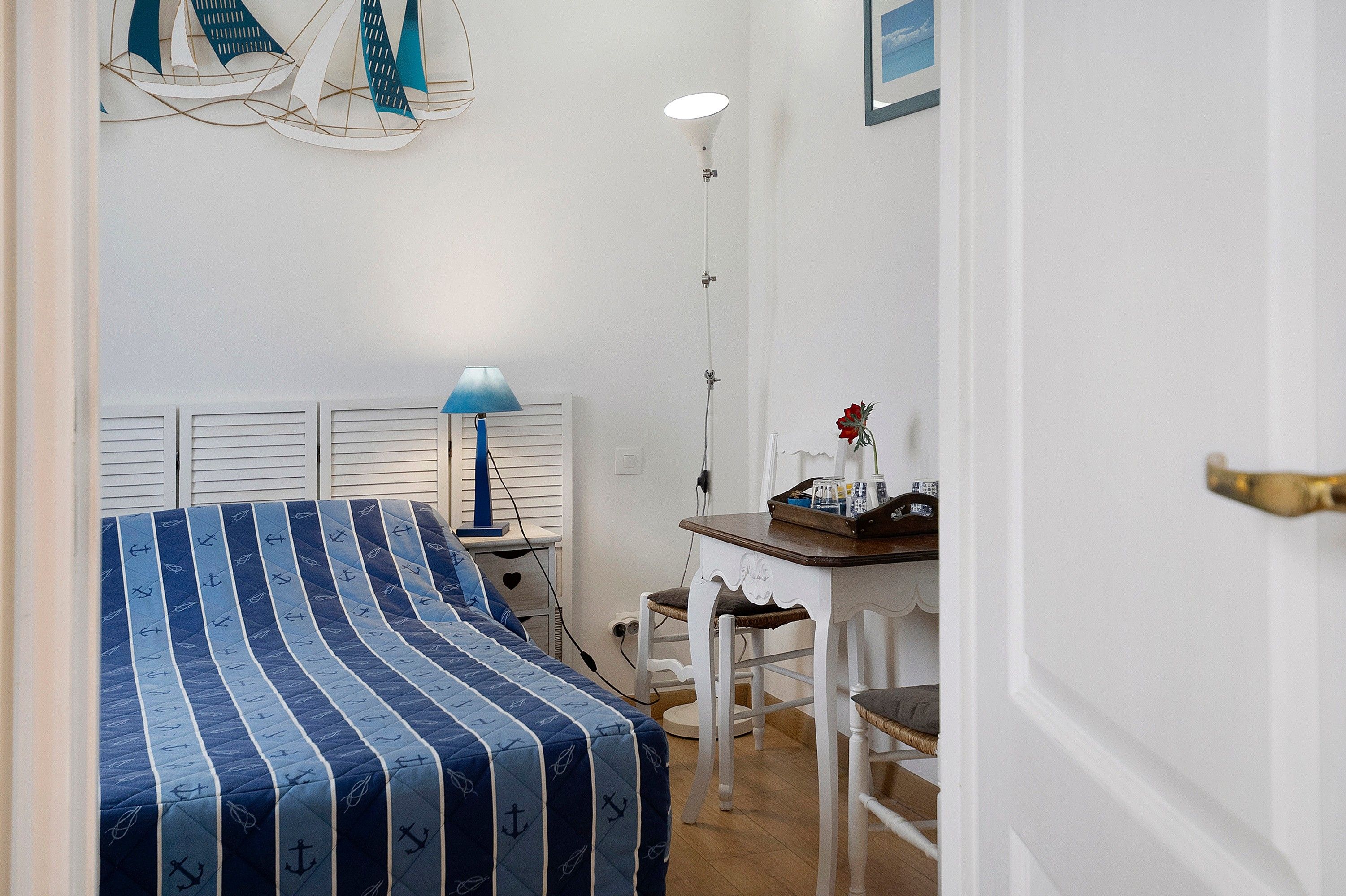 Un dormitorio con una cama, una mesita de noche, una lámpara, una silla y una pequeña mesa con un florero.