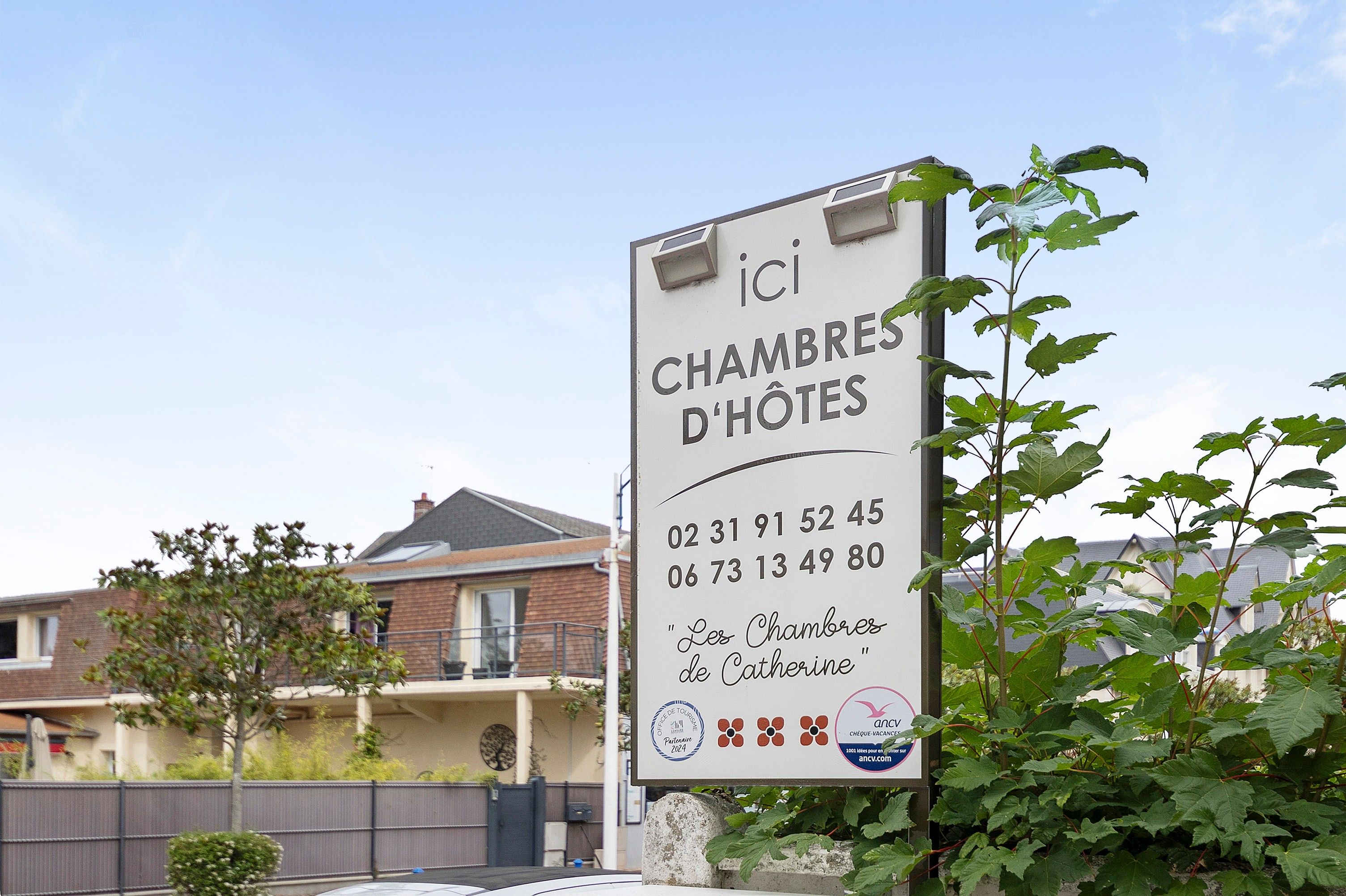 Letrero del hotel 'Les Chambres de Catherine' con números de contacto y un logotipo.