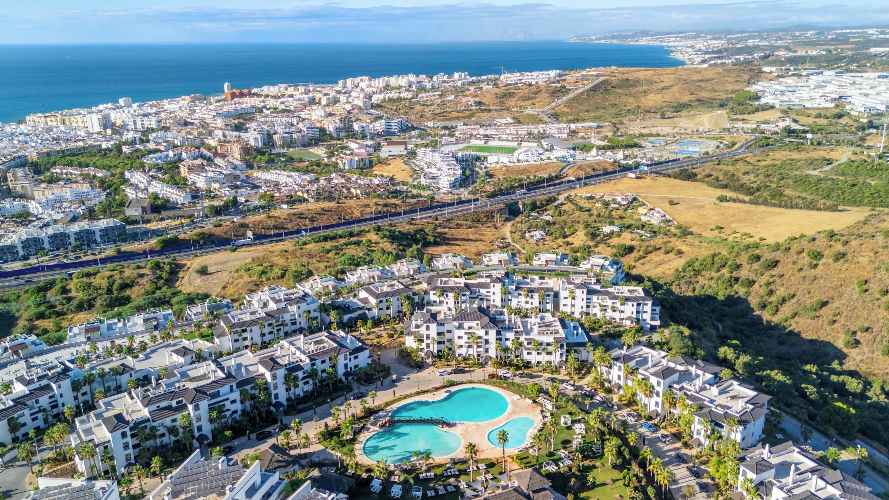Vista aèria d'una zona residencial a la costa amb una gran piscina envoltada d'edificis moderns.