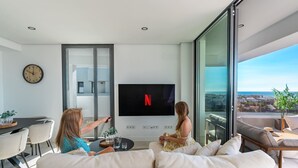 A modern living room with a large flat-screen TV mounted on the wall, a sofa, and a dining area with chairs. - Mirador Estepona Hills 15 | Pool & Private Jacuzzi (Estepona)