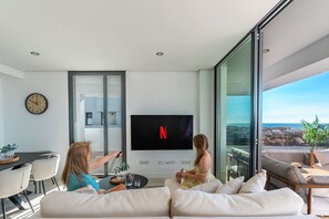 Ein modernes Wohnzimmer mit großem Flachbildfernseher an der Wand, einer Couch und einem Essbereich mit Stühlen.