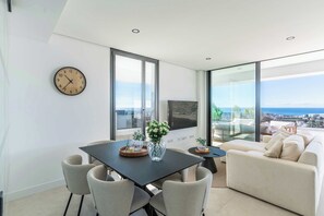 Ein modernes Wohnzimmer mit Essbereich, großen Fenstern, einer Uhr und Blick auf die Stadt.