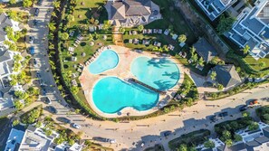 Luchtbeeld van een resort met meerdere zwembaden, een brug en veel groen in de omgeving.