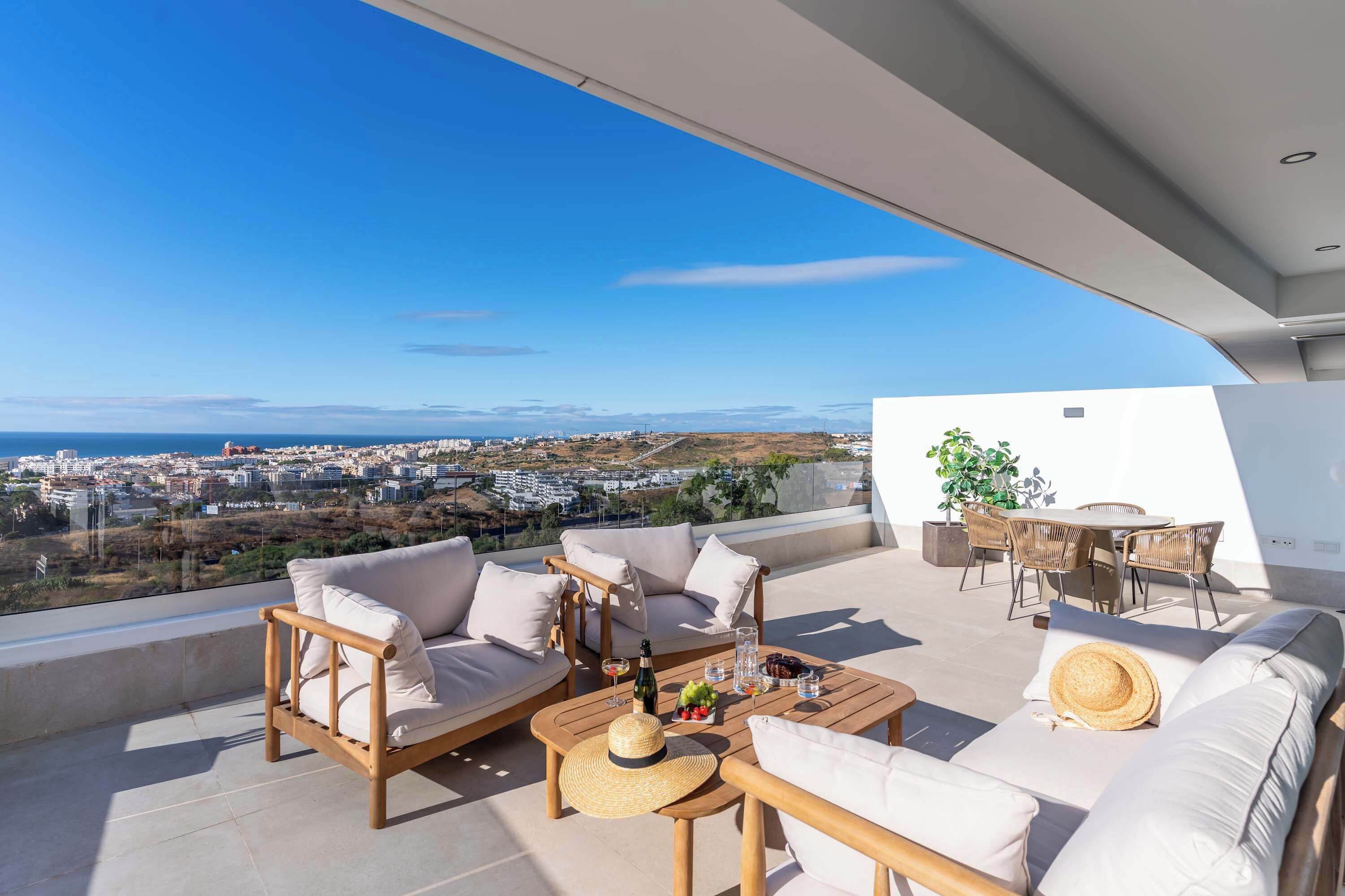 A spacious balcony with a sofa, chairs, and a dining table, overlooking a cityscape.