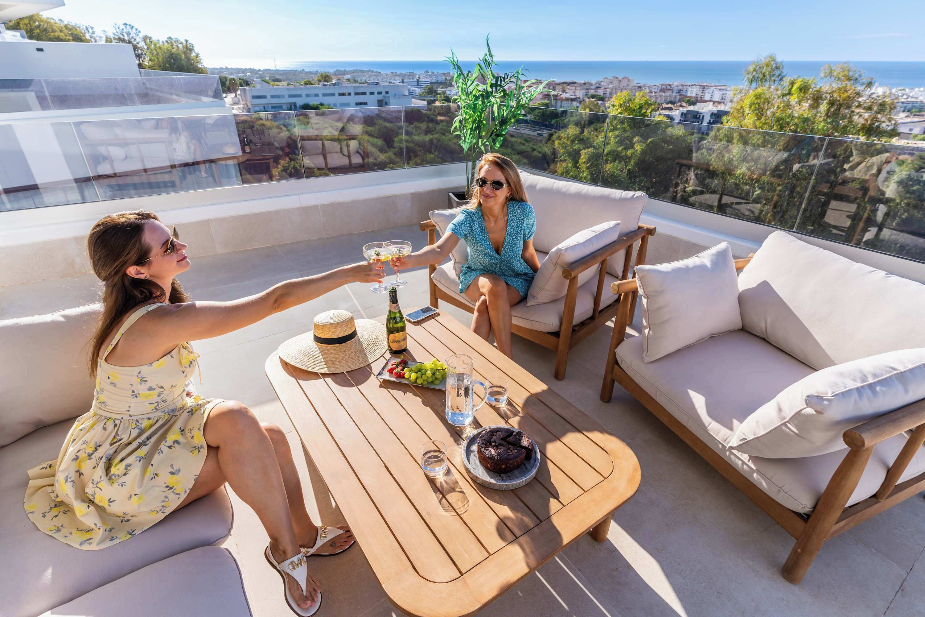 Zwei Personen sitzen auf einem Balkon mit einem Tisch, einer Flasche und einer Schale mit Trauben.
