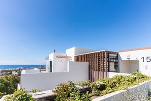 Een modern gebouw met een witte gevel, een houten pergola en uitzicht op zee.