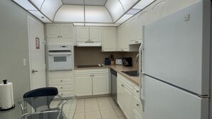 Cozinha compacta com armários brancos, geladeira, micro-ondas e cafeteira.