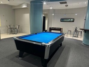 Ein Billardtisch in einem Raum mit an der Wand montiertem Flachbildfernseher, einem Sessel und einem kleinen Tisch.