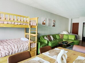 Ein Zimmer mit Etagenbetten, einem grünen Sofa, einem Esstisch und Bildern an der Wand.