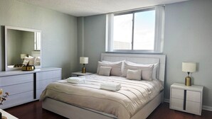 Quarto de hotel com cama grande, mesas de cabeceira, espelho e janela.