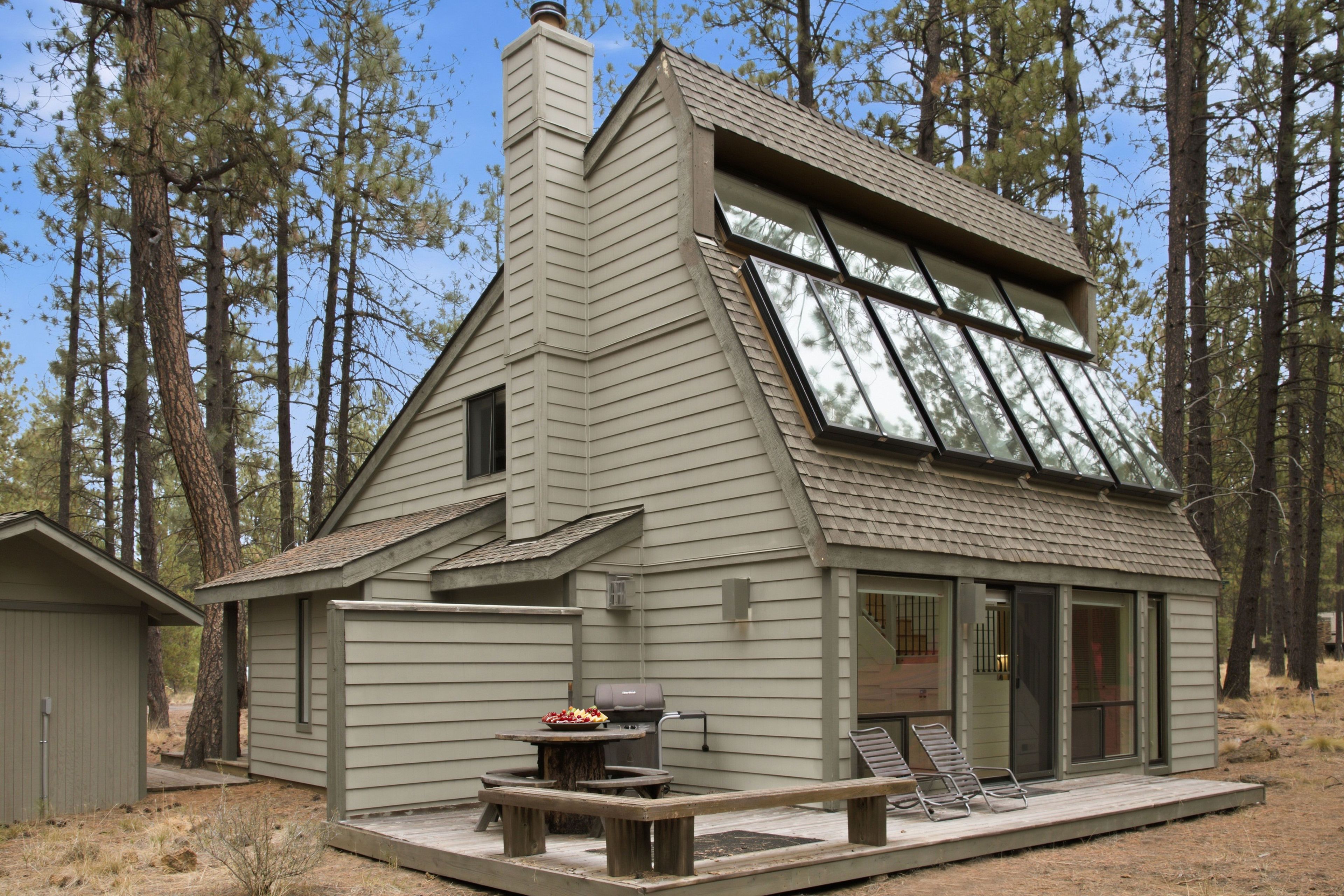 Cabin exterior featuring a wooded backdrop, large angled roof windows, and a rear deck.