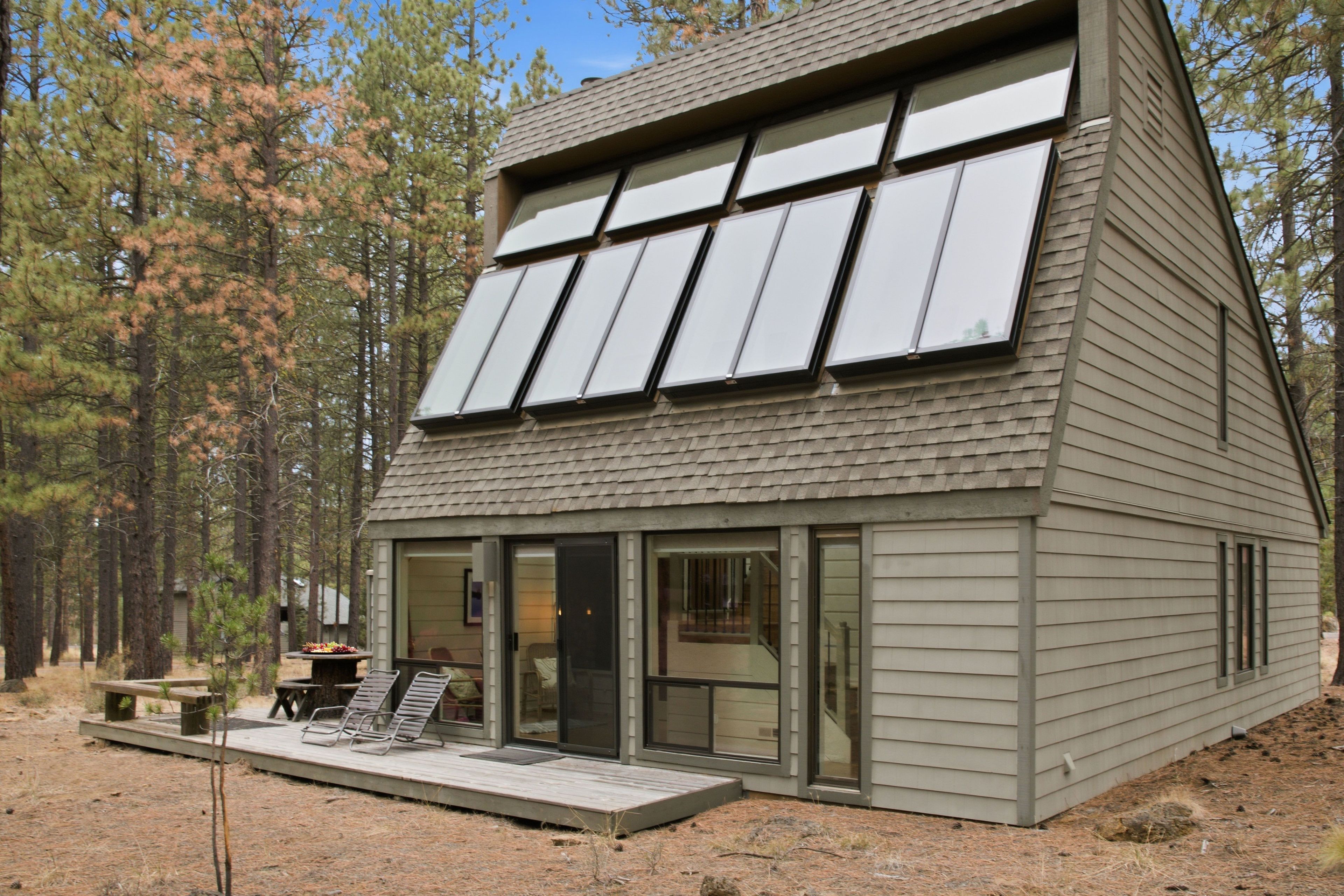 A modern house with a sloped roof, large windows, and a deck with outdoor furniture.