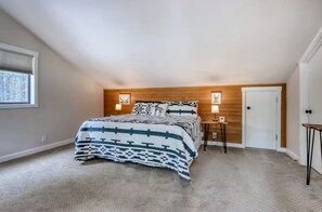 A bedroom with a bed, a nightstand, a door, and a window. - Sunriver Home – SHARC Passes, Bikes, EV Charger (Sunriver)