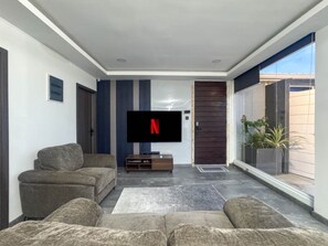 A modern living room with a flat-screen TV, two sofas, a coffee table, and a sliding glass door leading to a balcony.