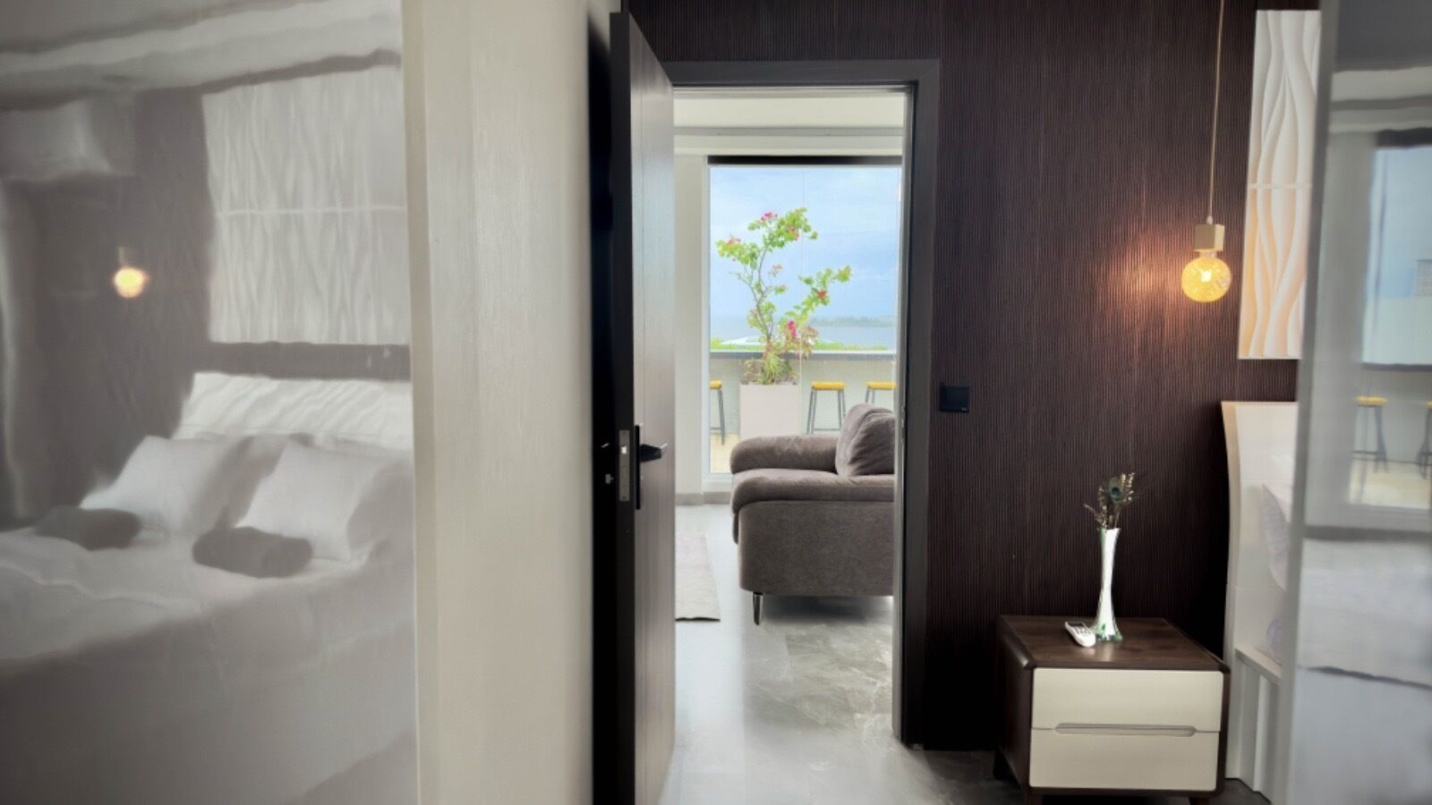 Une chambre d’hôtel avec un lit, une table de chevet ornée d’un vase, un canapé et une vue sur l’extérieur.