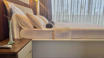 A hotel room with a bed, a nightstand with a lamp, and a vase with dried plants.