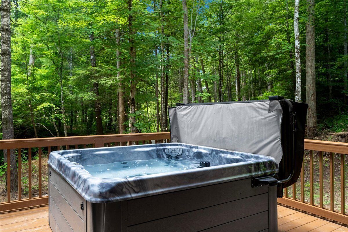 Een hottub op een houten terras, omringd door een bos.