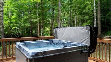 Een hottub op een houten terras, omringd door een bos.