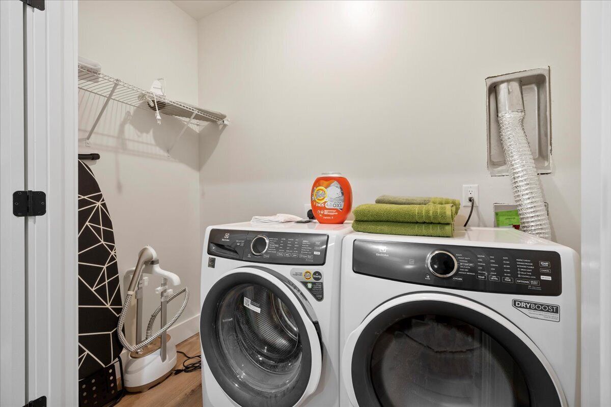 A laundry area with two washing machines, a drying machine, a hanging rack, and a towel.
