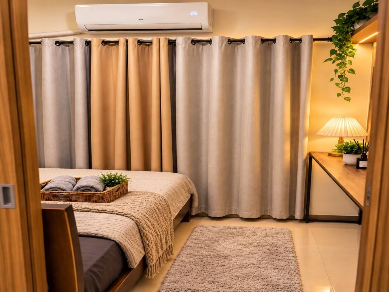 A bedroom with a bed, a bedside table with a lamp, a wall-mounted air conditioner, and a window with curtains.
