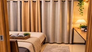 A bedroom with a bed, a bedside table with a lamp, a wall-mounted air conditioner, and a window with curtains.