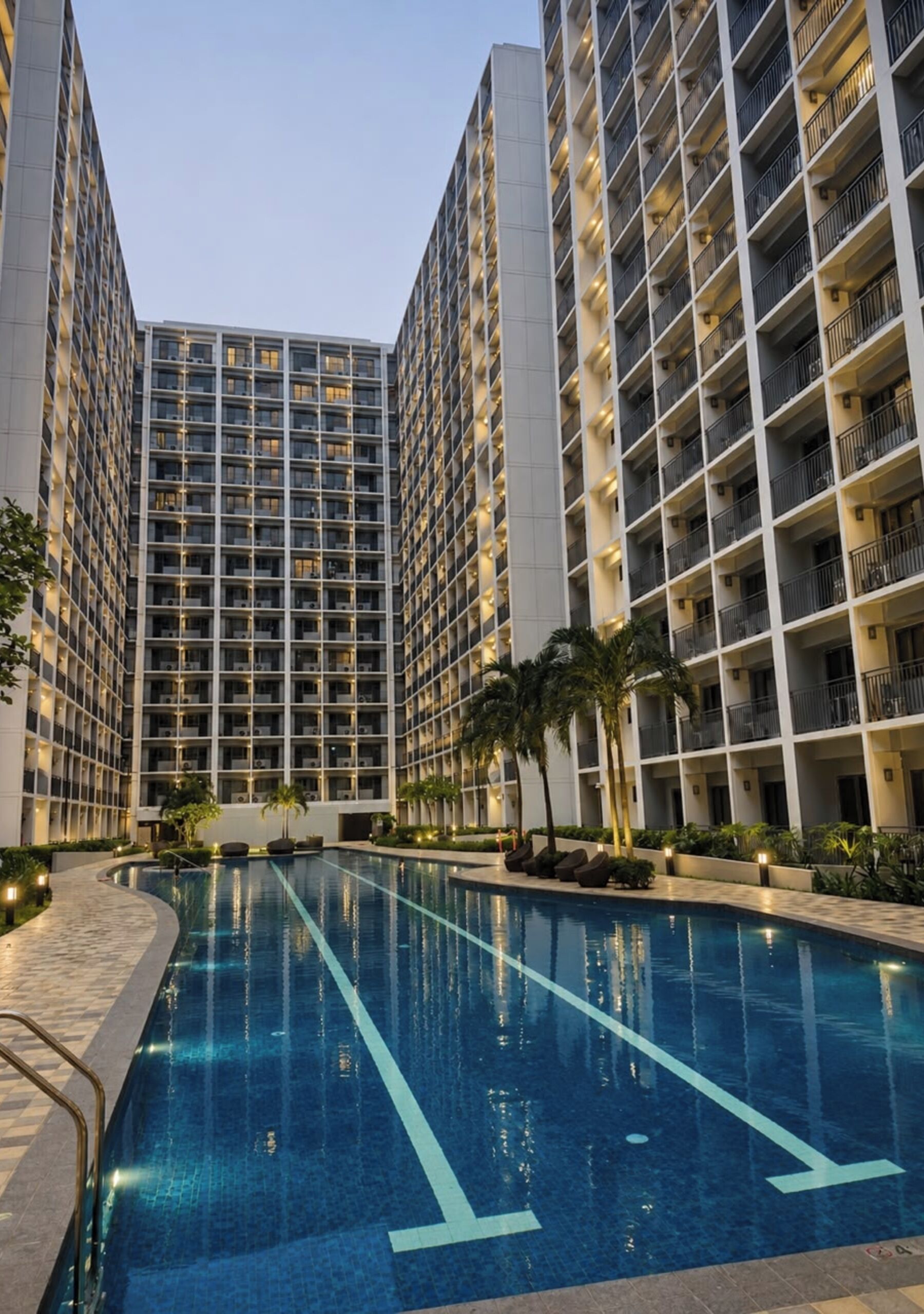 A modern hotel with a central swimming pool, high-rise buildings, and a well-lit exterior.