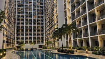 A modern hotel with a central swimming pool, high-rise buildings, and a well-lit exterior.