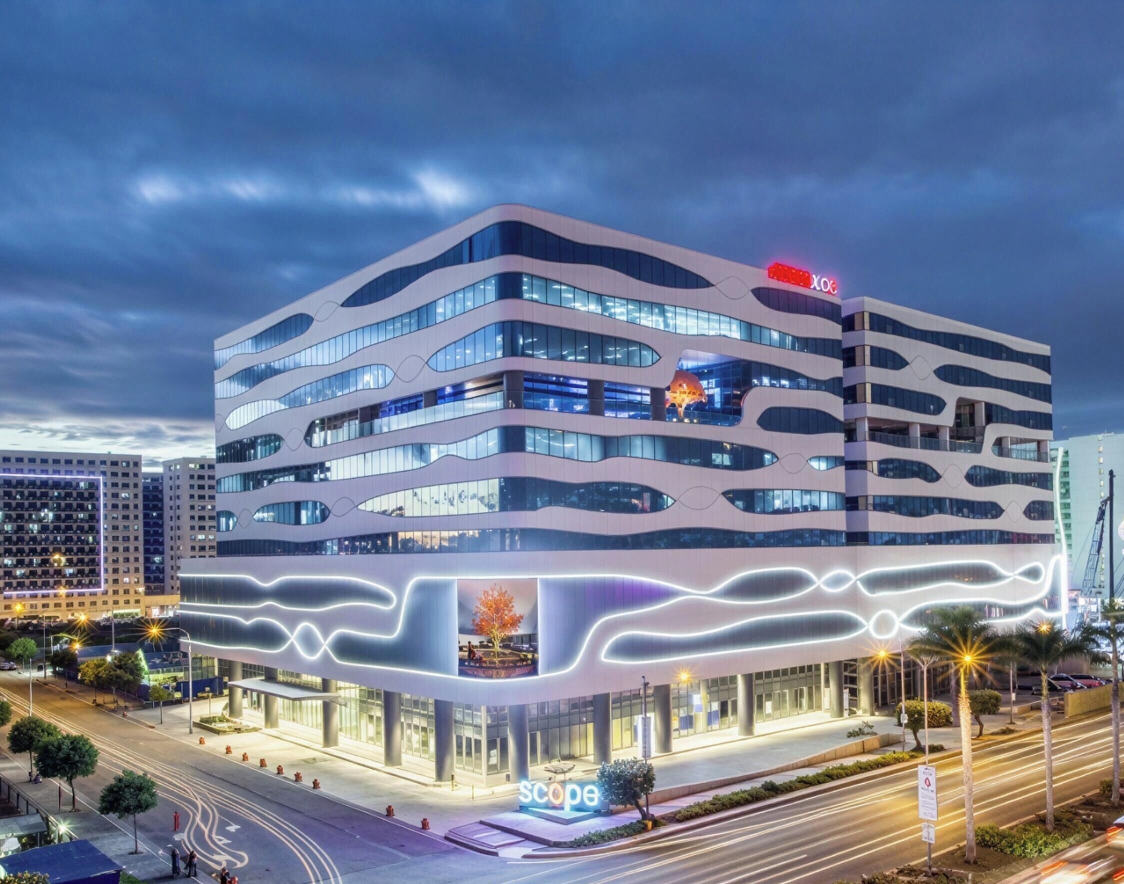 A multi-story building with a modern architectural design, featuring a prominent 'XOX' sign on the top.