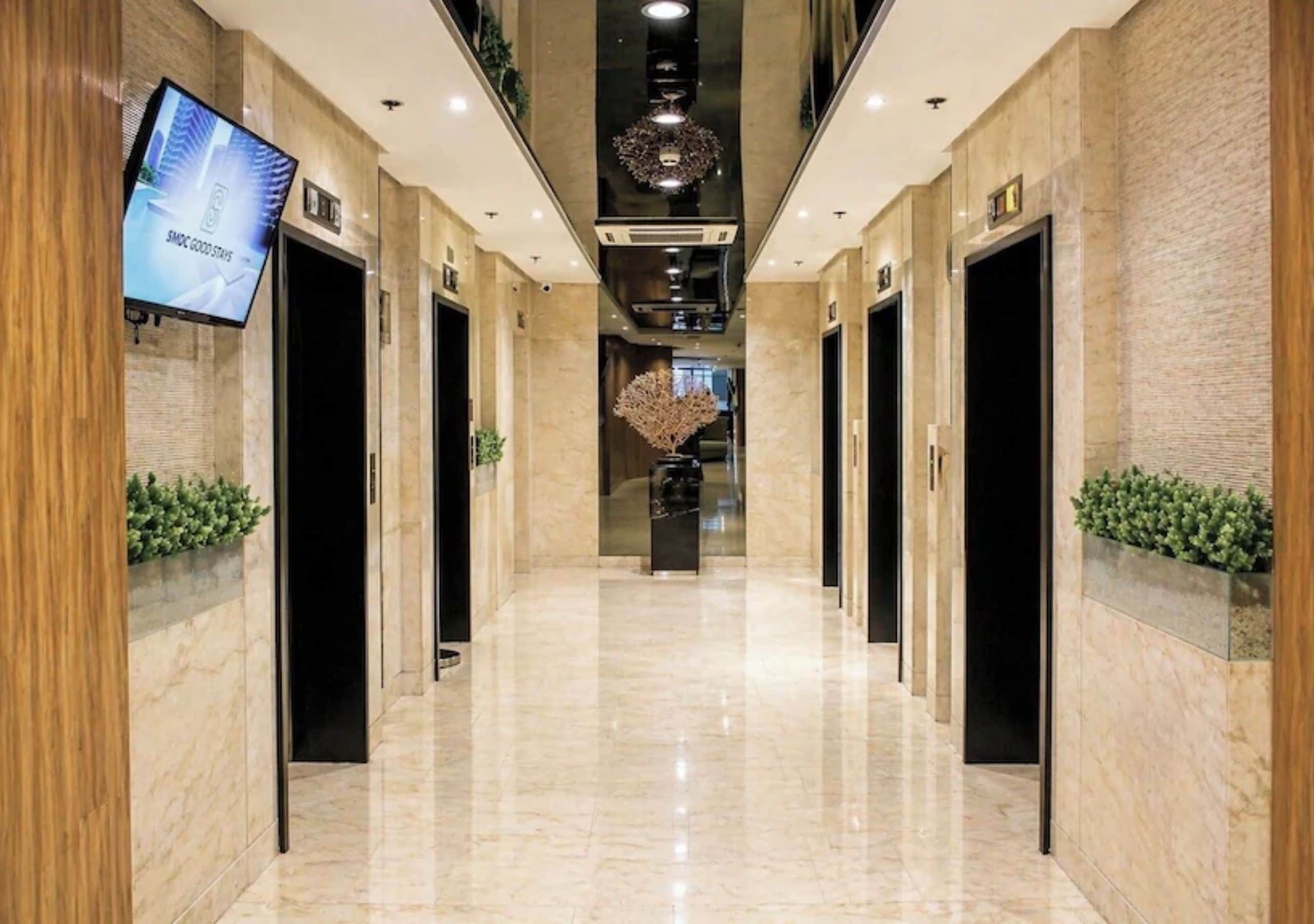 A hotel corridor with marble flooring, wooden paneling, and a television screen displaying a message.