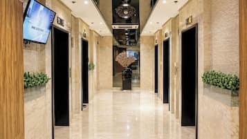 A hotel corridor with marble flooring, wooden paneling, and a television screen displaying a message.
