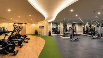 Ein modernes Fitnessstudio mit Herz-Kreislauf-Geräten, Krafttrainingsmaschinen und einem Teppichbereich in Grün.