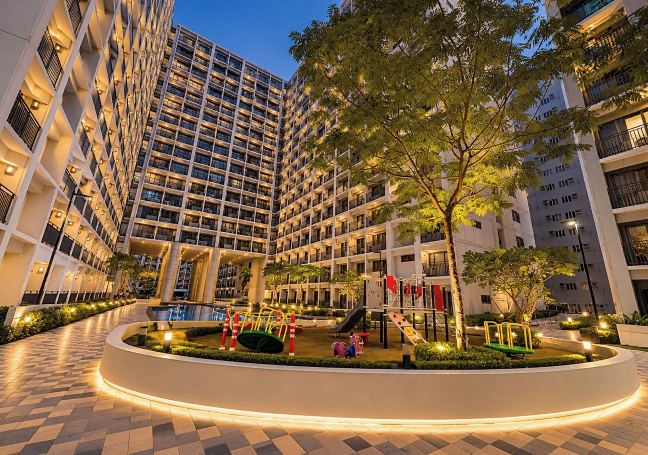 Un hotel de varios pisos con un patio central que incluye un parque infantil, rodeado de edificios altos.