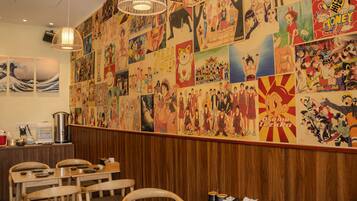 Ein Restaurantinnenraum mit einer Wand, die mit verschiedenen Anime- und Manga-Postern, Holztischen und hängenden Lampen dekoriert ist.