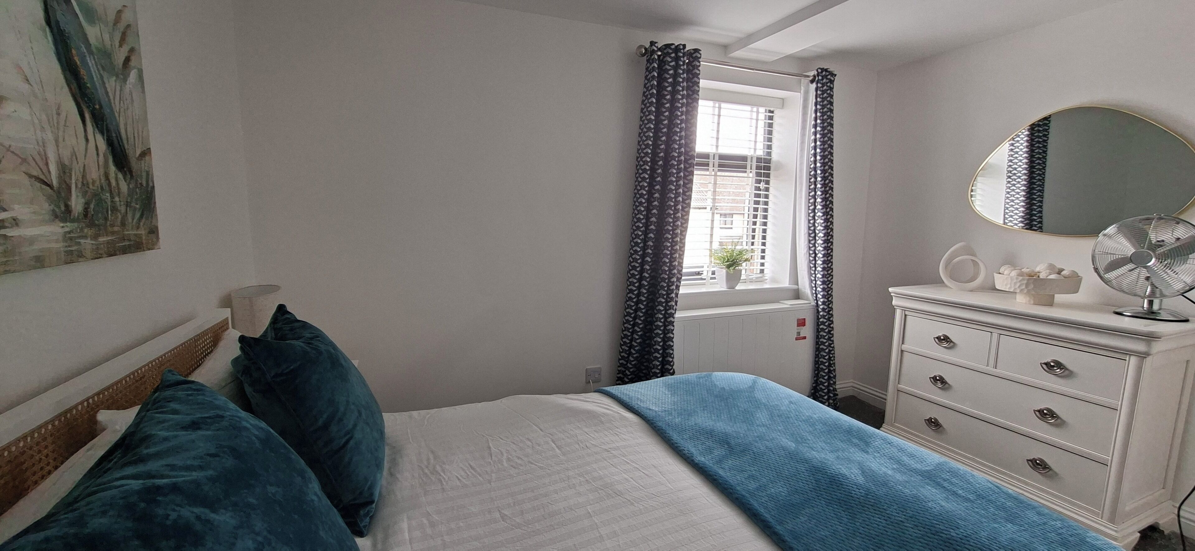 A bedroom with a bed, a dresser, a mirror, and a window with curtains.