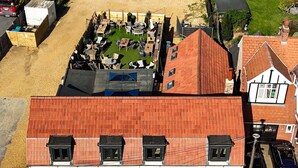 A multi-story building with a red-tiled roof, multiple windows, and a parking area with cars.