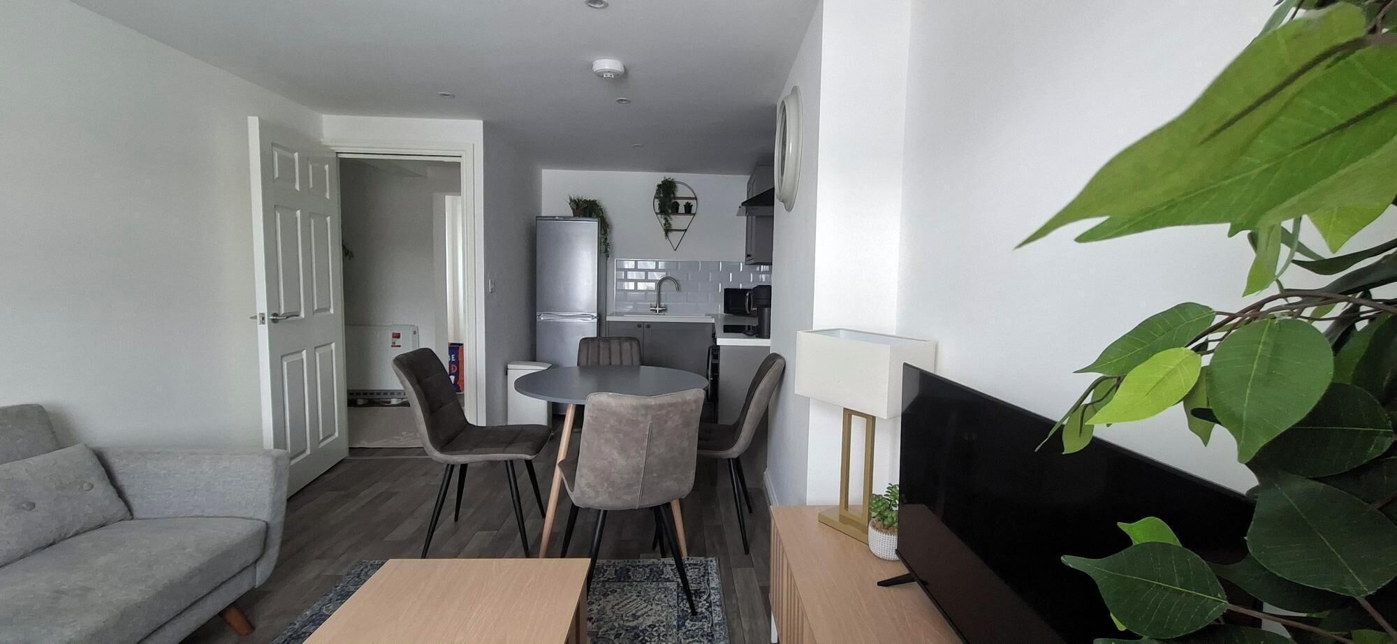 A compact living space with a dining area, kitchenette, and a grey sofa.