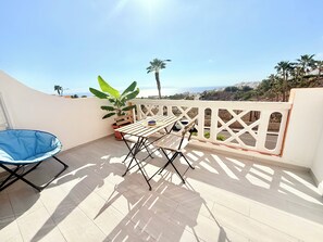 Un balcon avec une table et des chaises, une chaise bleue, une plante en pot et une vue sur la mer.