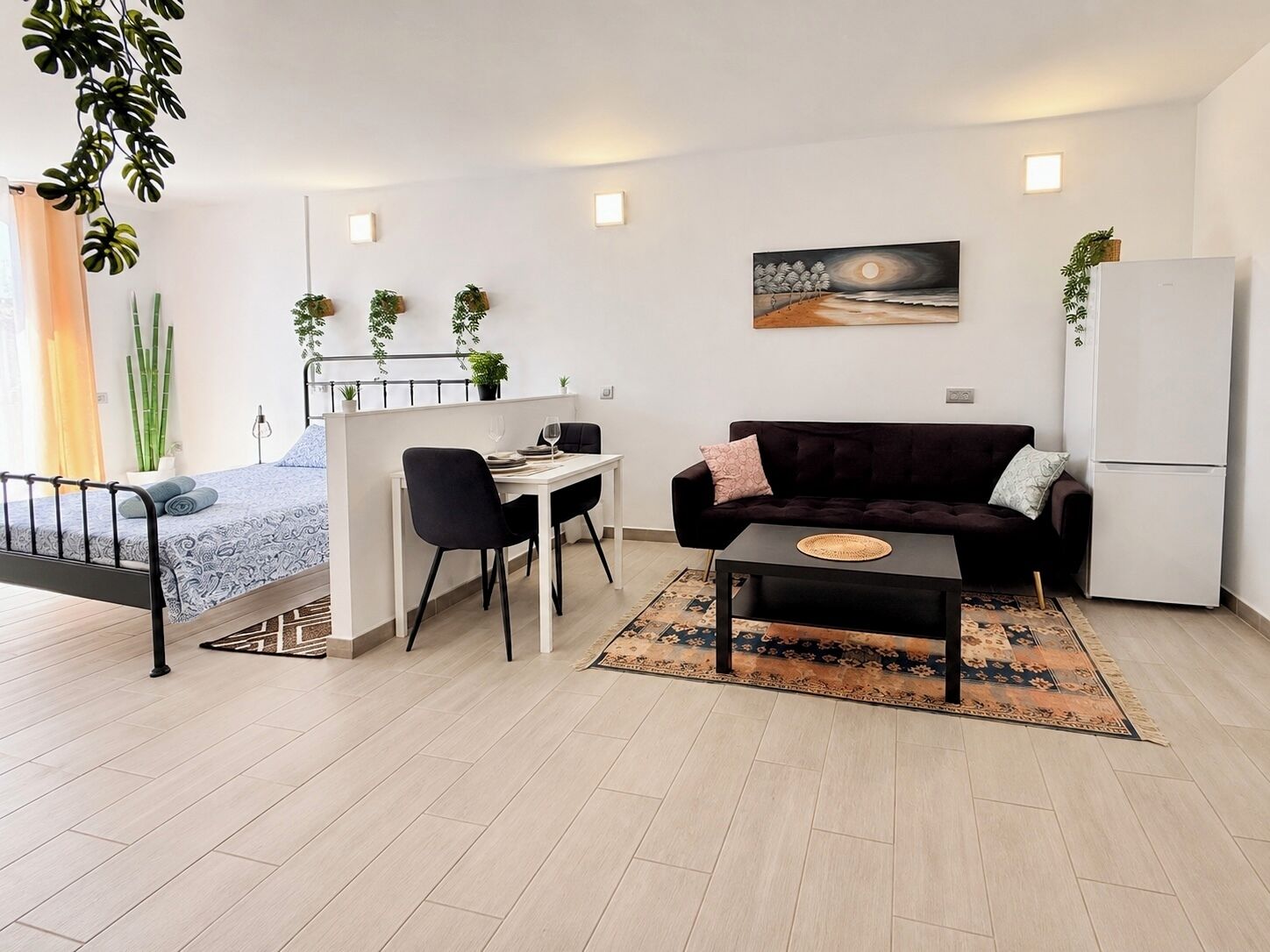 Een moderne woonruimte met een bed, een eethoek, een bank en een koelkast.