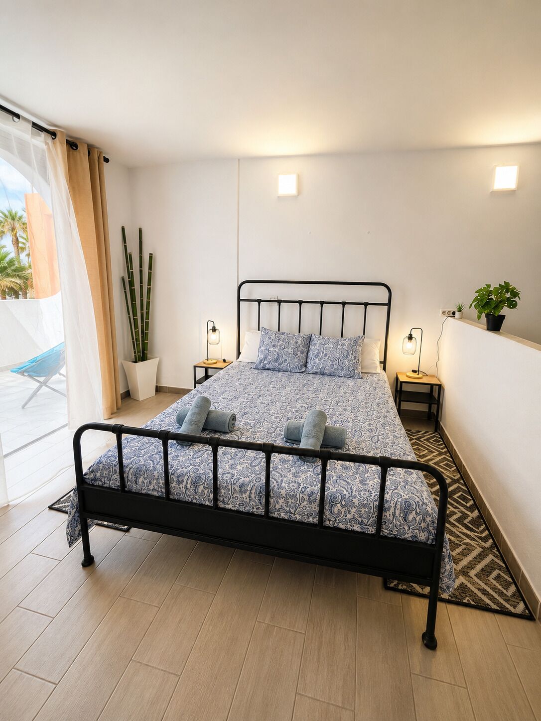 Een moderne slaapkamer met een bed, bedlampen, een potplant en uitzicht op het buiten.