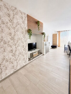 Una sala de estar moderna con pared de mármol, televisor de pantalla plana, techo de listones de madera y comedor con mesa y sillas.