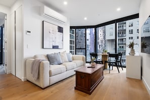A modern living room with a sofa, coffee table, and a large window offering a city view. - High-rise 1-bed Apartment Near Docklands (Melbourne)