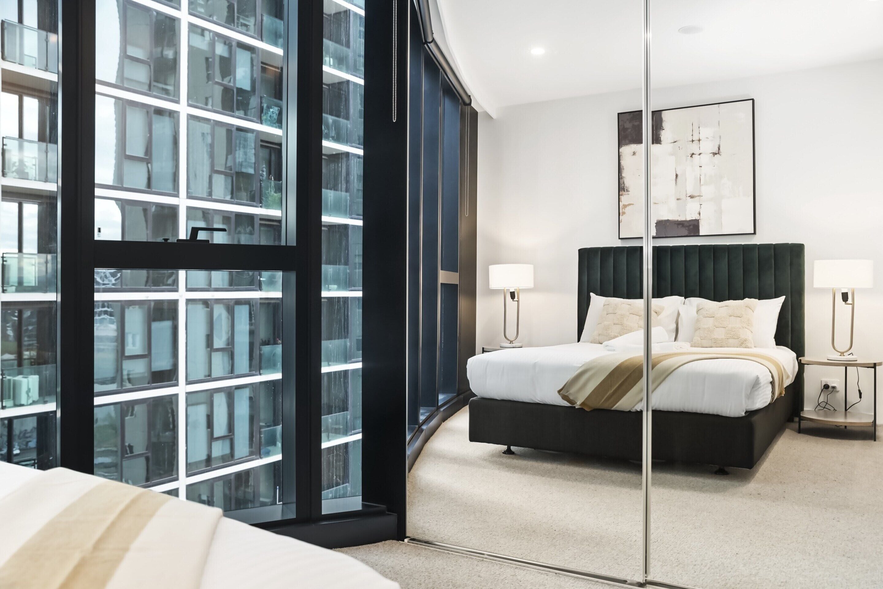 Ein modernes Hotelzimmer mit einem großen Bett, Nachttischen, einem Wandbild und Blick durch eine Glastür.