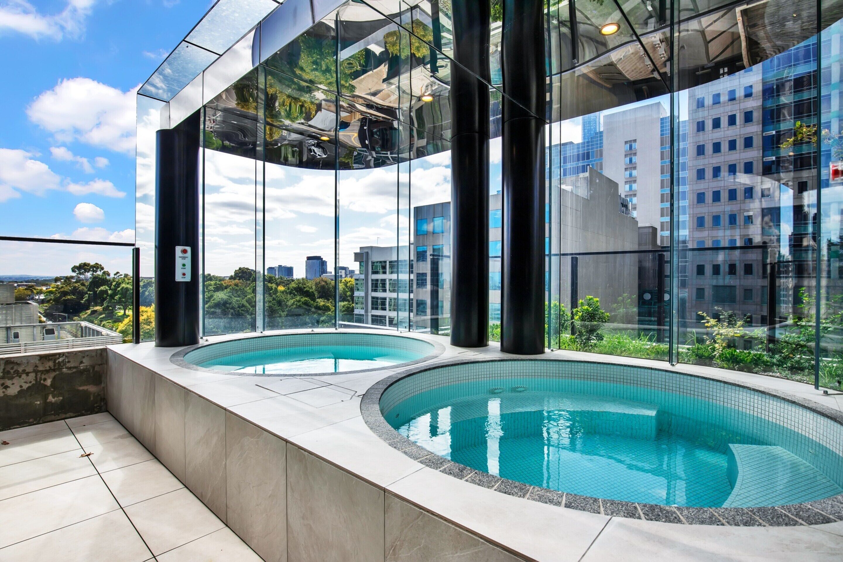 A modern building with two outdoor swimming pools, large glass windows, and a view of the cityscape.