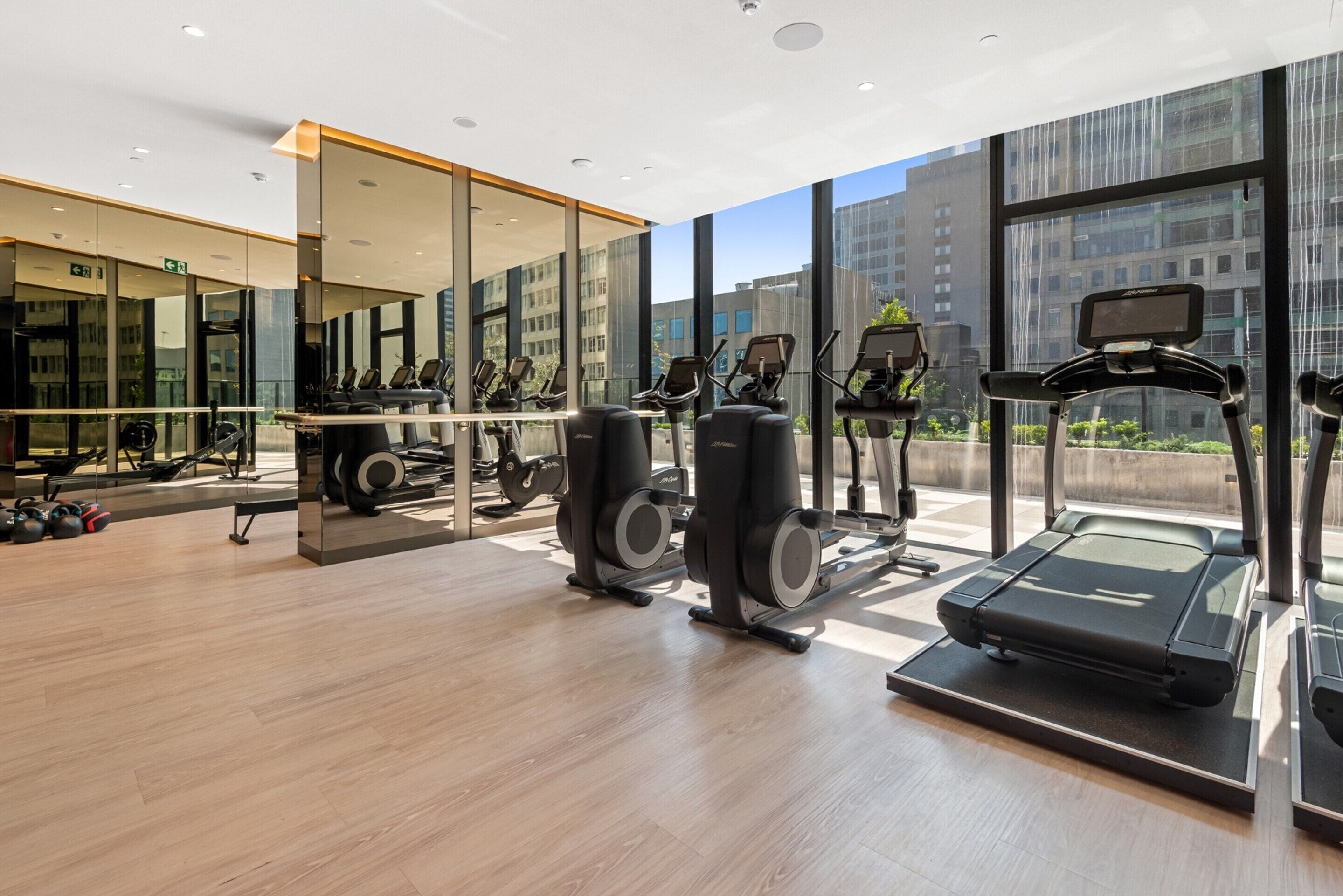 Una palestra moderna con macchinari cardio, attrezzature per l'allenamento con i pesi e un ampio specchio che riflette l'ambiente.