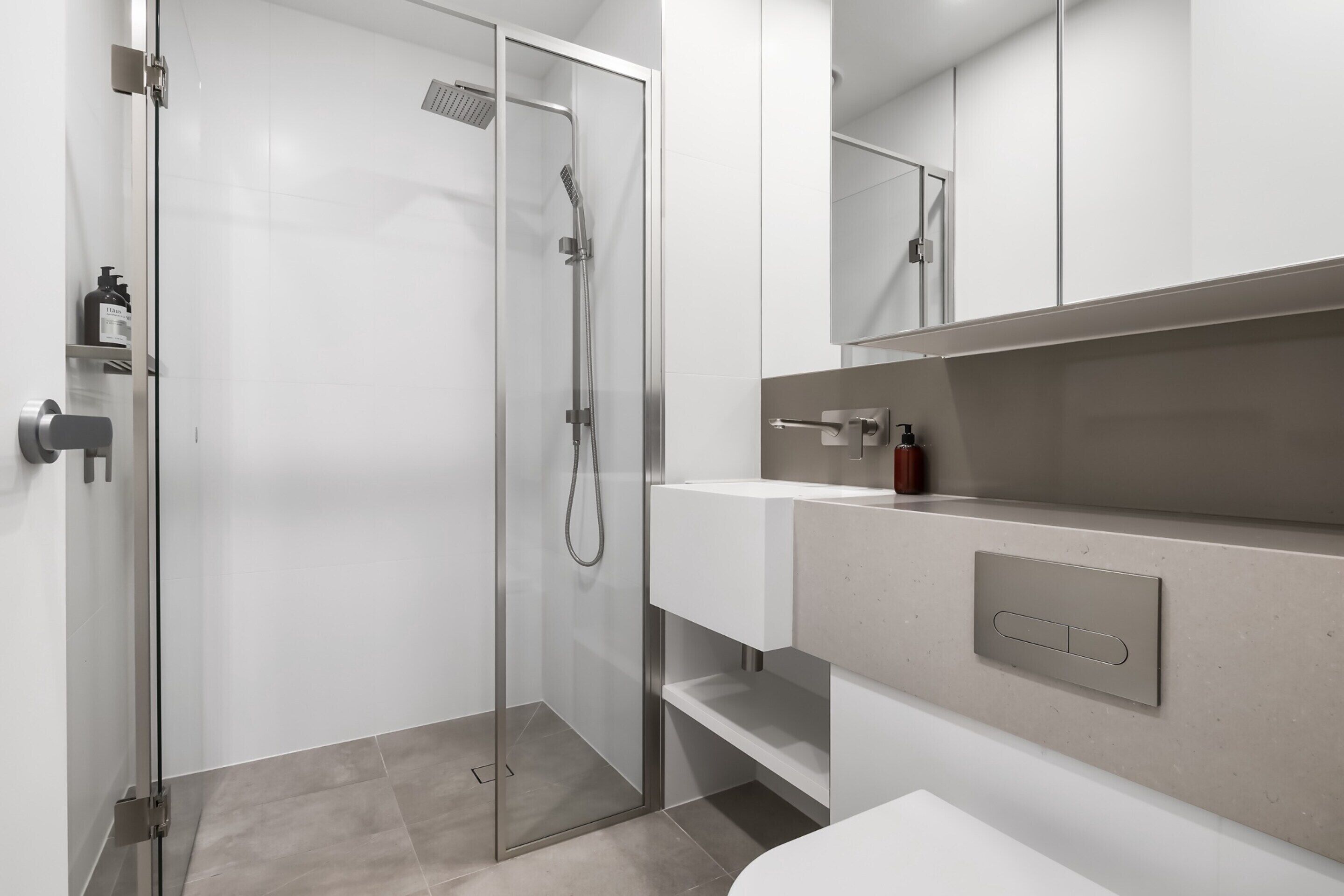 A modern bathroom with a glass-enclosed shower, a white sink, and a mirror above the vanity.