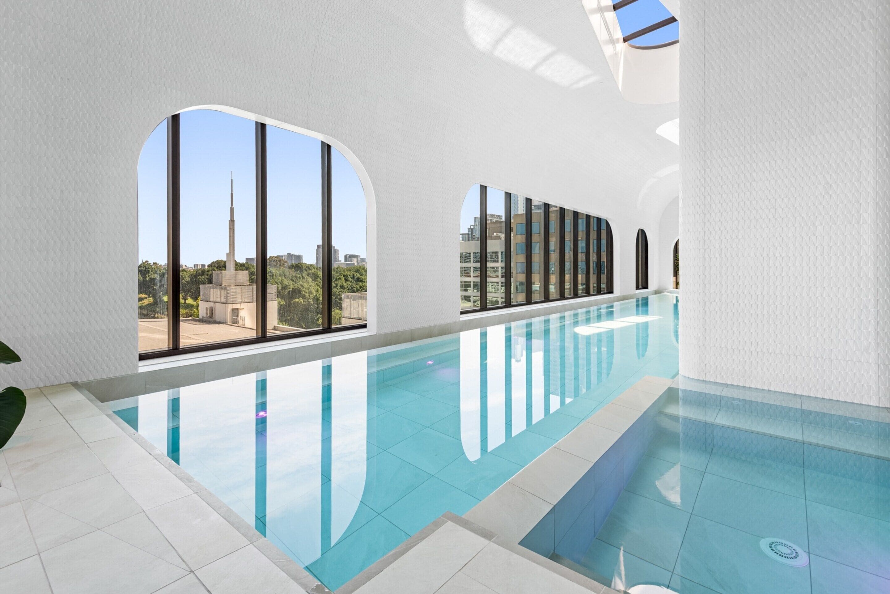 Una piscina interna moderna con ampie finestre ad arco e vista sulla città.