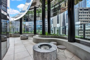 A modern outdoor lounge area with a circular seating arrangement, large windows, and a view of surrounding buildings. - High-rise 1-bed Apartment Near Docklands (Melbourne)
