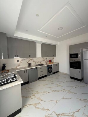 A modern kitchen with grey cabinets, a built-in dishwasher, a microwave, and a stainless steel refrigerator. - Villa Younes (Djerba Midun)