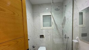 A modern bathroom with a wooden door, a white toilet, a glass-enclosed shower, and a large mirror. - Villa Younes (Djerba Midun)